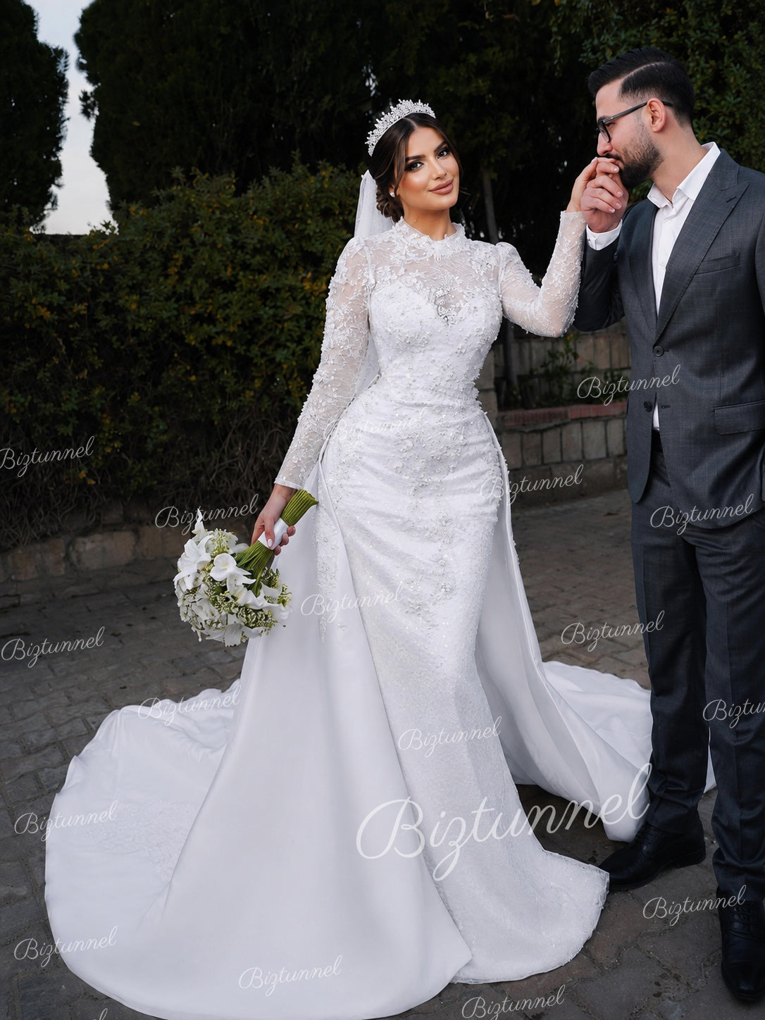 Woman in a white wedding dress holding a bouquet, standing next to a man in formal attire.