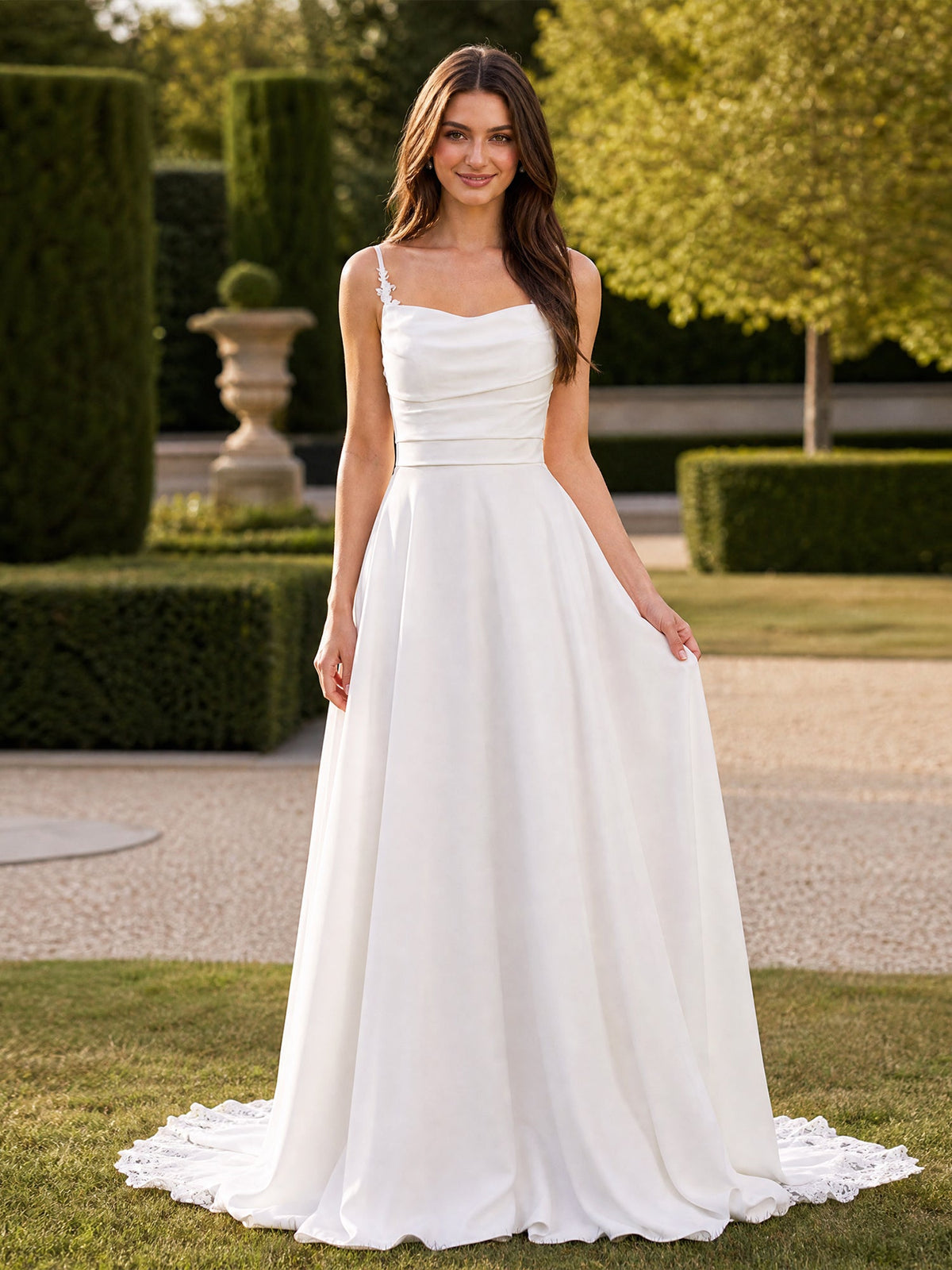 White A-line wedding dress with spaghetti straps, a ruched draped bodice, and a full floor-length skirt with lace appliqué at the hem, front view.
